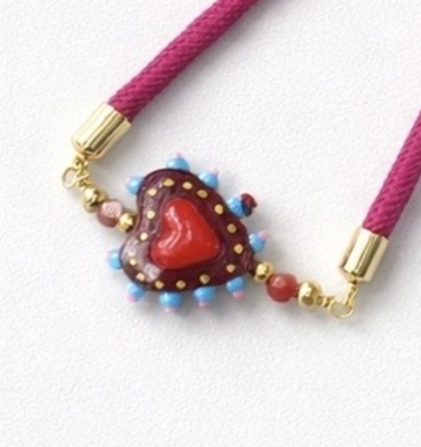 Un collar hecho a mano con cordón magenta y colgante en forma de corazón con detalles en rojo, azul y dorado combina a la perfección con nuestra Pulsera Corazón de cristal con cordón azul.