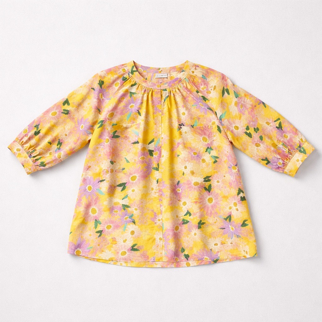 Vestido amarillo de manga larga para niña con un colorido estampado floral de flores rosas, moradas y naranjas y hojas verdes, sobre un fondo blanco liso.