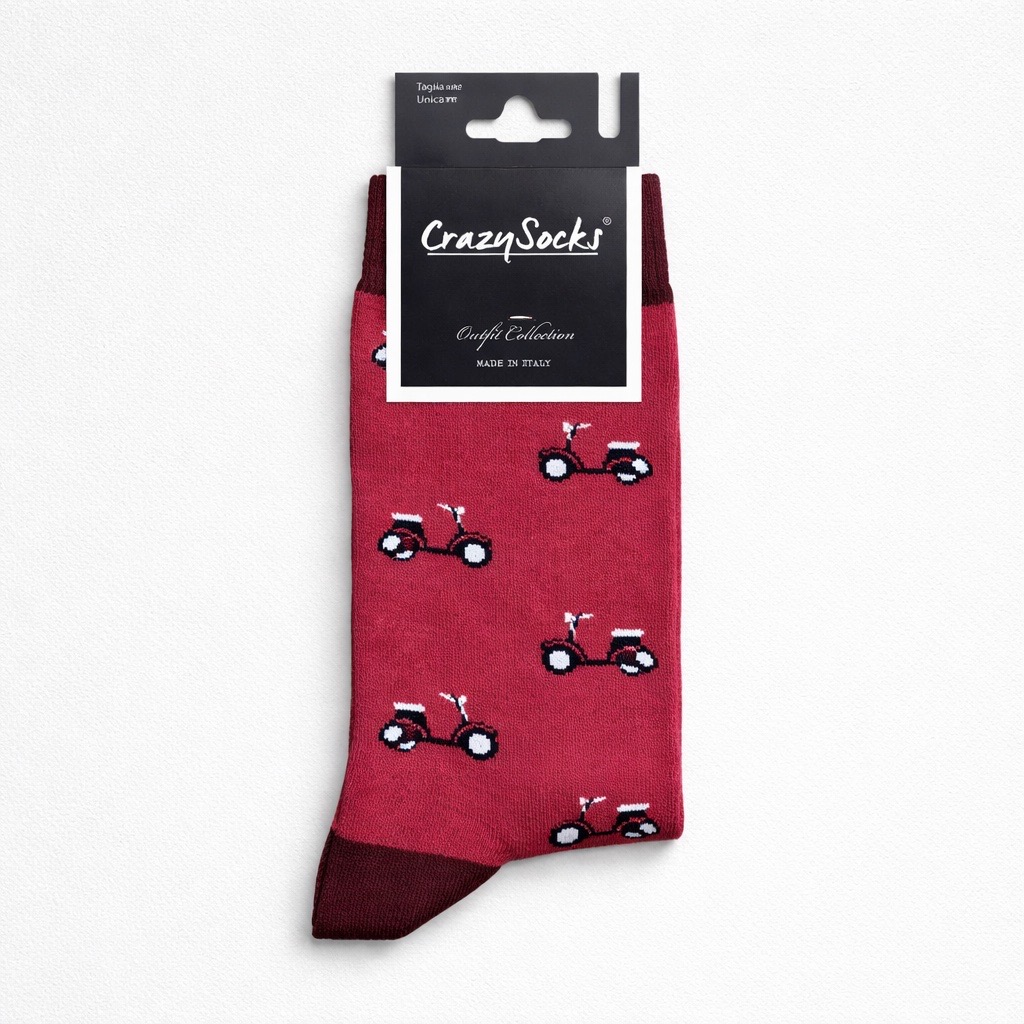 Un par de calcetines rojos Crazy Socks con un dibujo repetido de pequeños patinetes, con punteras y puños de color rojo oscuro, presentados sobre fondo blanco en su embalaje original.