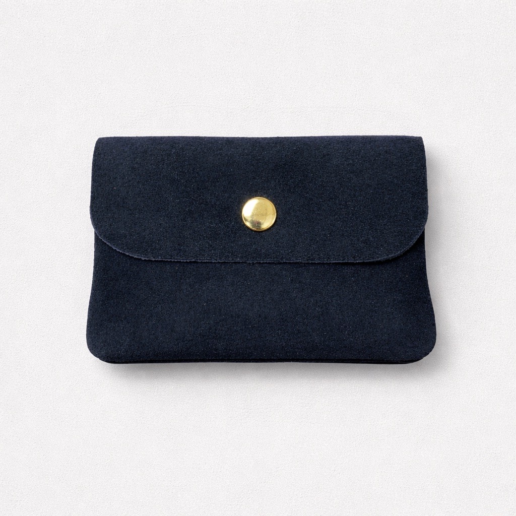 Pequeña bolsa rectangular de ante azul marino con solapa sujeta por un botón de presión redondo dorado, colocada sobre un fondo claro liso.