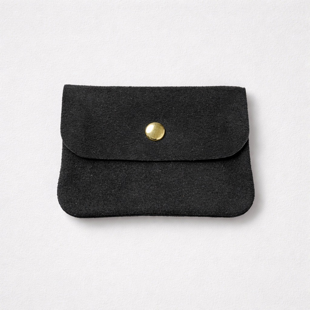 Una pequeña bolsa de ante negro con solapa sujeta por un único botón de presión redondo dorado, sobre un fondo blanco liso.