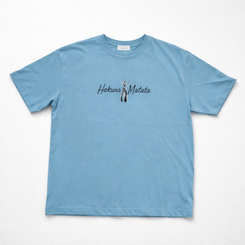La Camiseta Oversize "Hakuna Matata" - Unisex - Azul | 100% Algodón presenta una ilustración de cuatro suricatas de pie juntas con "Hakuna Matata" escrito sobre ellas en la espalda.