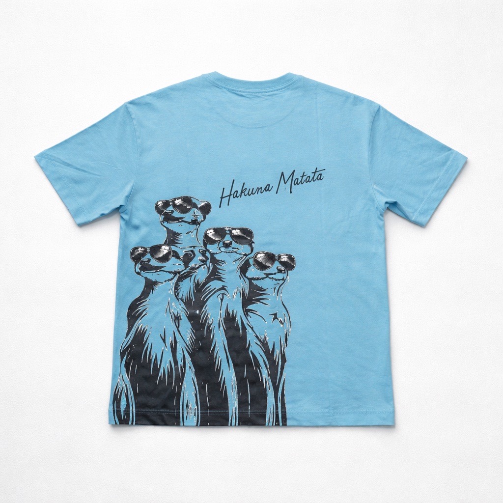 La Camiseta Oversize "Hakuna Matata" - Unisex - Azul | 100% Algodón presenta una ilustración de cuatro suricatas de pie juntas con "Hakuna Matata" escrito sobre ellas en la espalda.