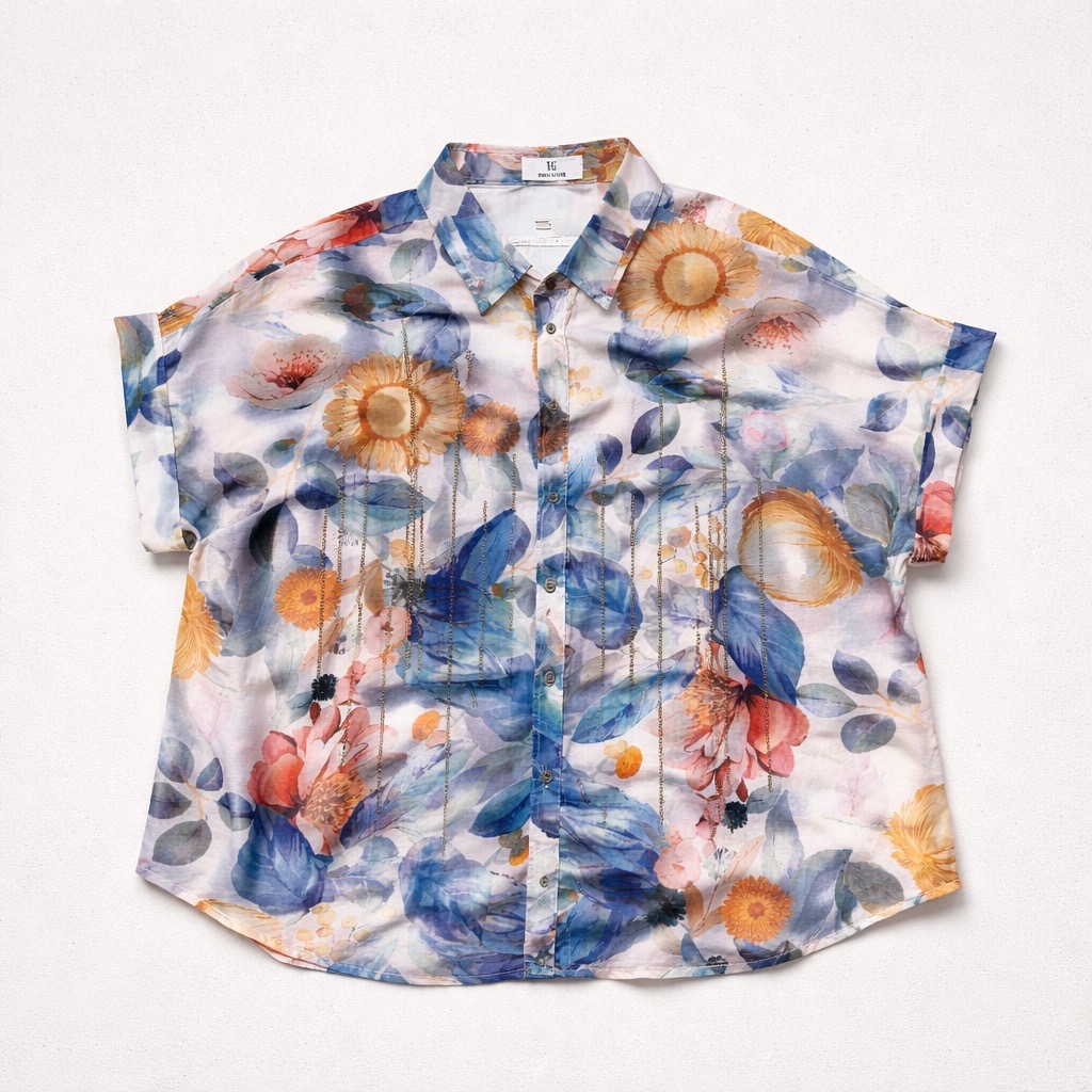 Blusa de manga corta con un colorido estampado floral y de hojas en tonos azules, amarillos, naranjas y rosas