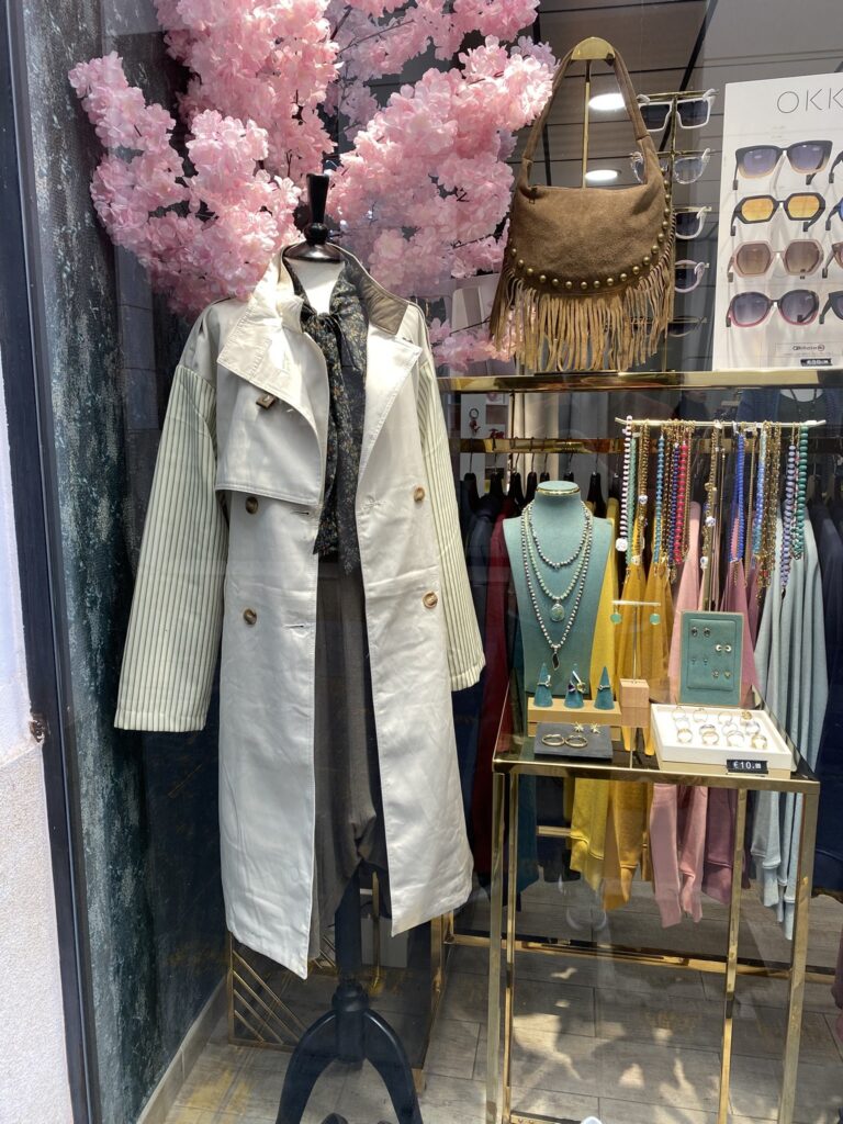 Escaparate de LYBA Store: gabardina y bisutería Detalle del escaparate de LYBA Store: gabardina de rayas, collares, anillos y pendientes, bolso de ante con flecos
