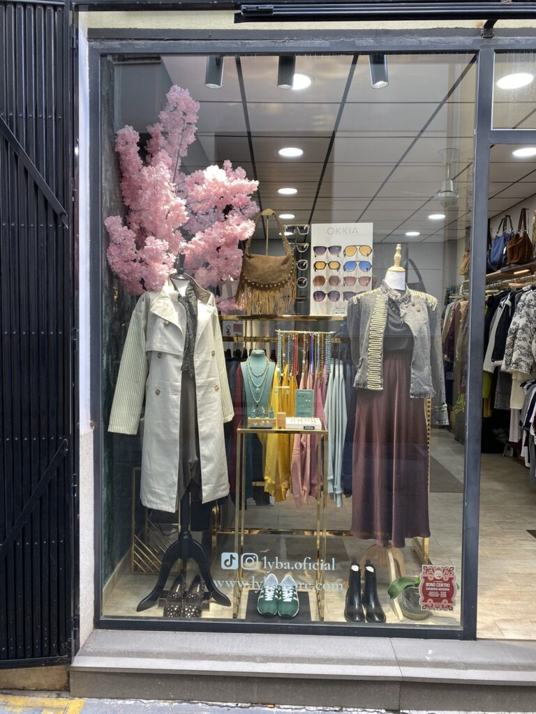Escaparate de otoño de LYBA Store en Valencia Escaparate de LYBA Store con gabardina, chaqueta militar, falda satinada, bisutería, bolso de flecos y gafas OKKIA
