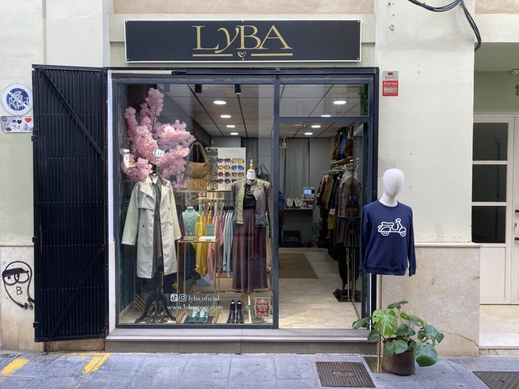 Entrada de LYBA Store en el centro de Valencia: rótulo dorado, escaparate con gabardina, chaqueta militar y gafas OKKIA