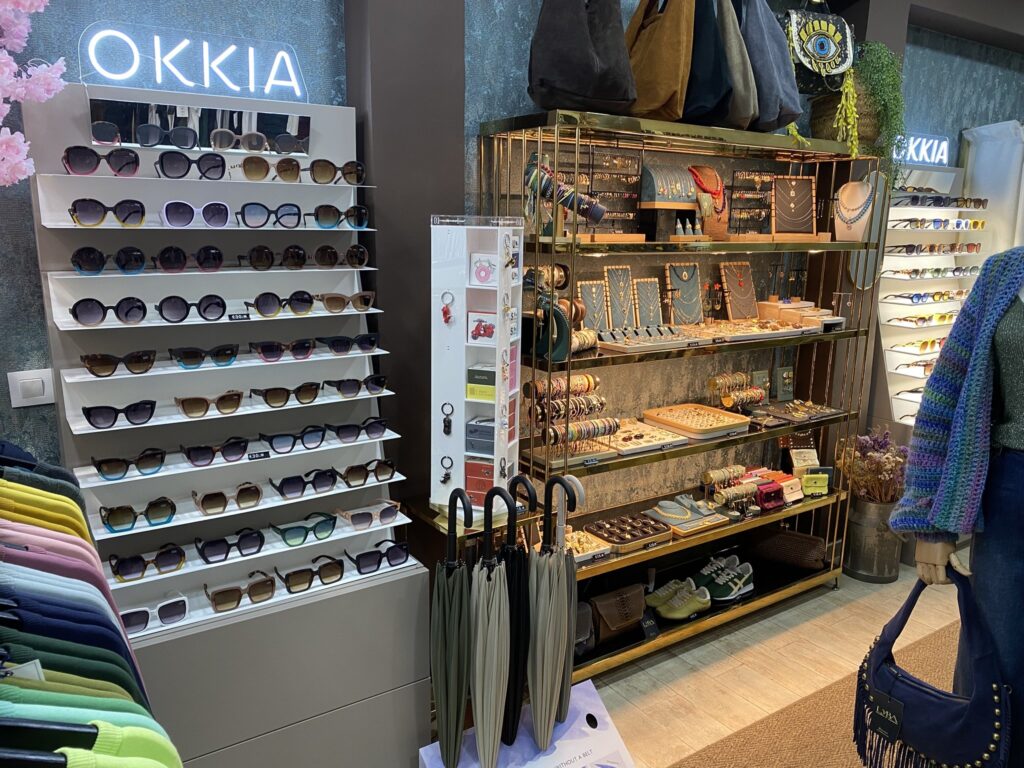 Interior de LYBA Store: expositor de gafas de sol OKKIA, estantería dorada con bisutería y paraguas Shupatto